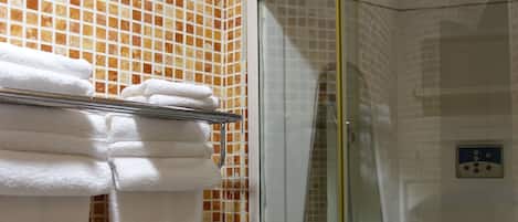 A bathroom with a glass-enclosed shower, a toilet, and a towel rack with folded towels.