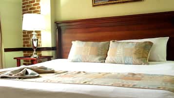 Cama bem arrumada com colcha, cabeceira de madeira e luminária em uma mesinha de cabeceira.