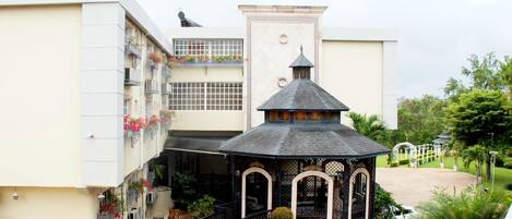 A building with a central tower, a covered outdoor area with a gazebo, and a balcony with flowers.