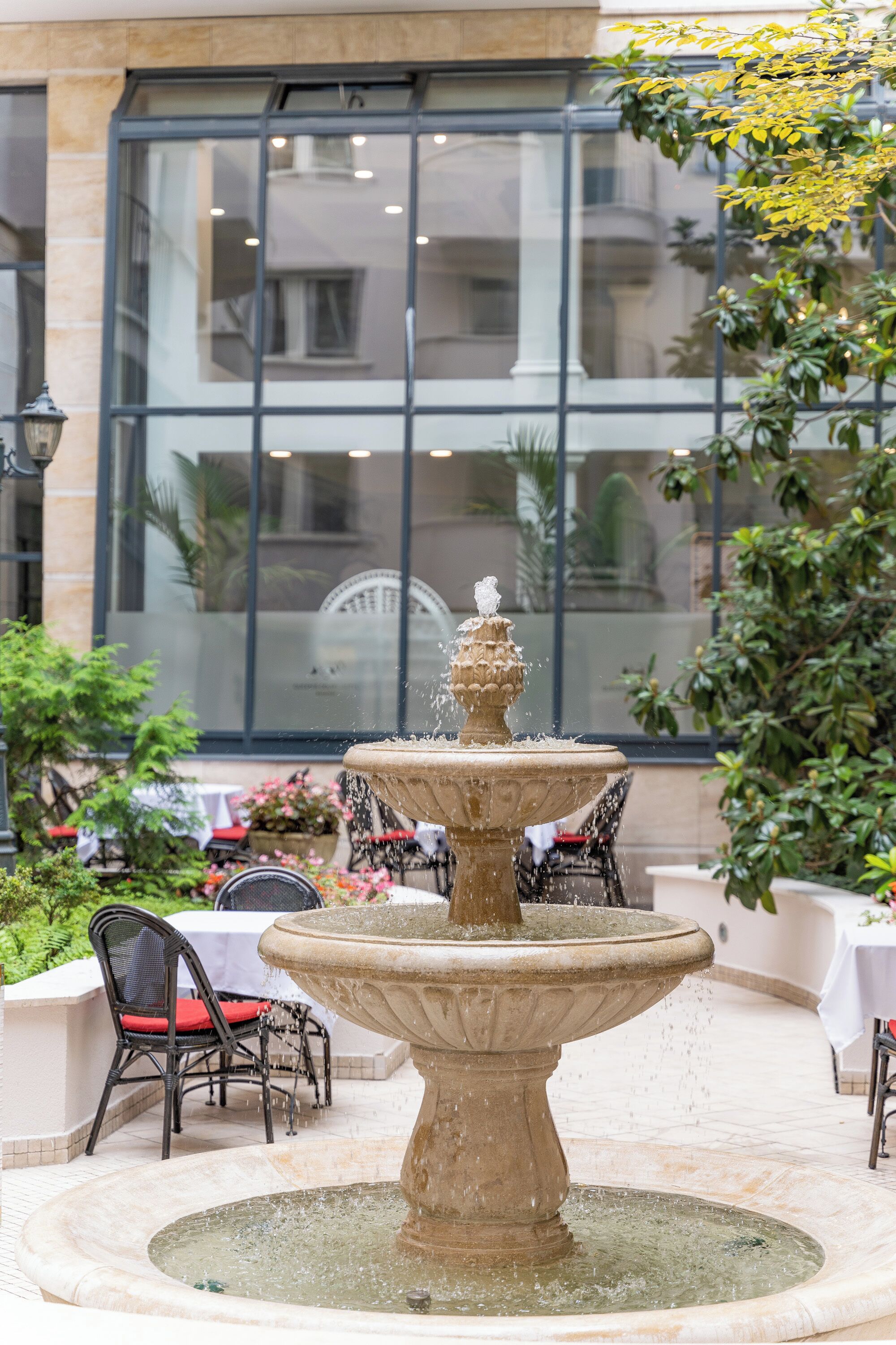 A stone fountain with water spouting from the top, surrounded by a tiled patio area with outdoor seating.