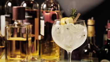 Un bar con una copa de cóctel adornada con una rodaja de limón y una ramita de romero, rodeada de diversas botellas de alcohol.