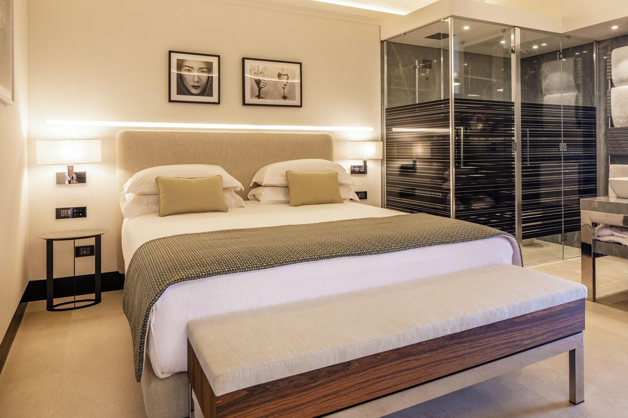 A modern hotel room with a large bed, bedside tables, a glass-enclosed shower, and artwork on the wall.