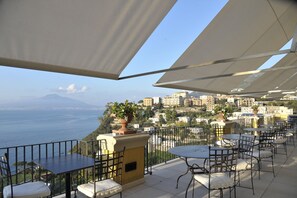 A terrace with outdoor seating, a view of the sea, and buildings in the background. - Grand Hotel Angiolieri (Vico Equense)