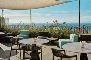 An outdoor seating area with round tables and chairs, a large umbrella, and a view of the sea. - Grand Hotel Angiolieri (Vico Equense)