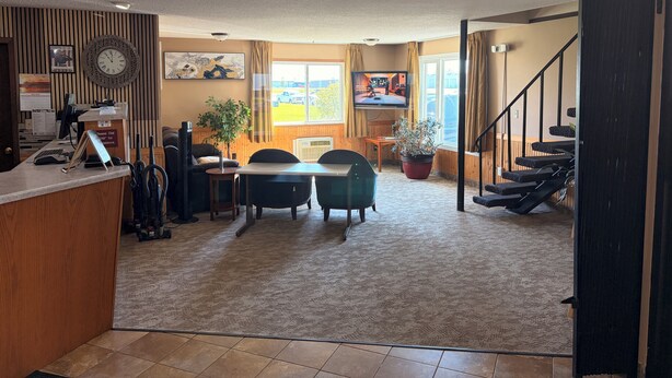 A spacious living area with a dining table, chairs, a TV, and a staircase. - East Grand Inn Grand Forks ND I 29 (East Grand Forks)