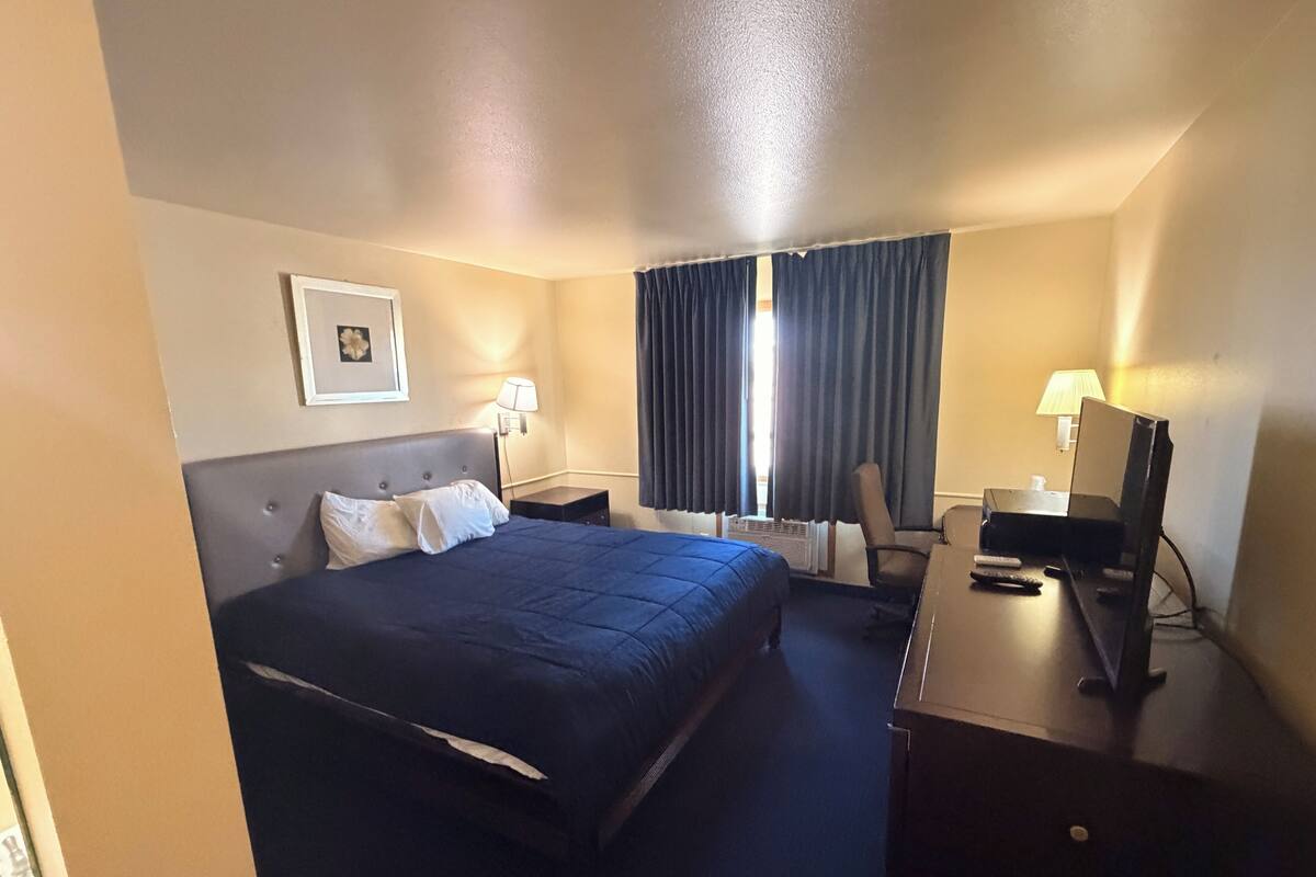 A hotel room with a bed, desk, chair, lamp, and a picture on the wall.