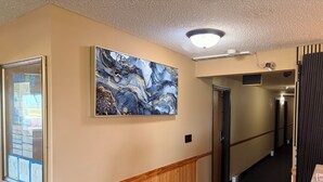 A hallway with a wooden wainscoting, a large abstract painting, a door, and a ceiling light fixture. - East Grand Inn Grand Forks ND I 29 (East Grand Forks)