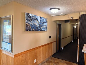A hallway with a wooden wainscoting, a large abstract painting, a door, and a ceiling light fixture. - East Grand Inn Grand Forks ND I 29 (East Grand Forks)