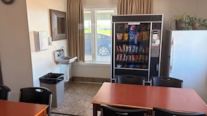A kitchenette with a sink, a window with curtains, a vending machine, and a table with chairs. - East Grand Inn Grand Forks ND I 29 (East Grand Forks)