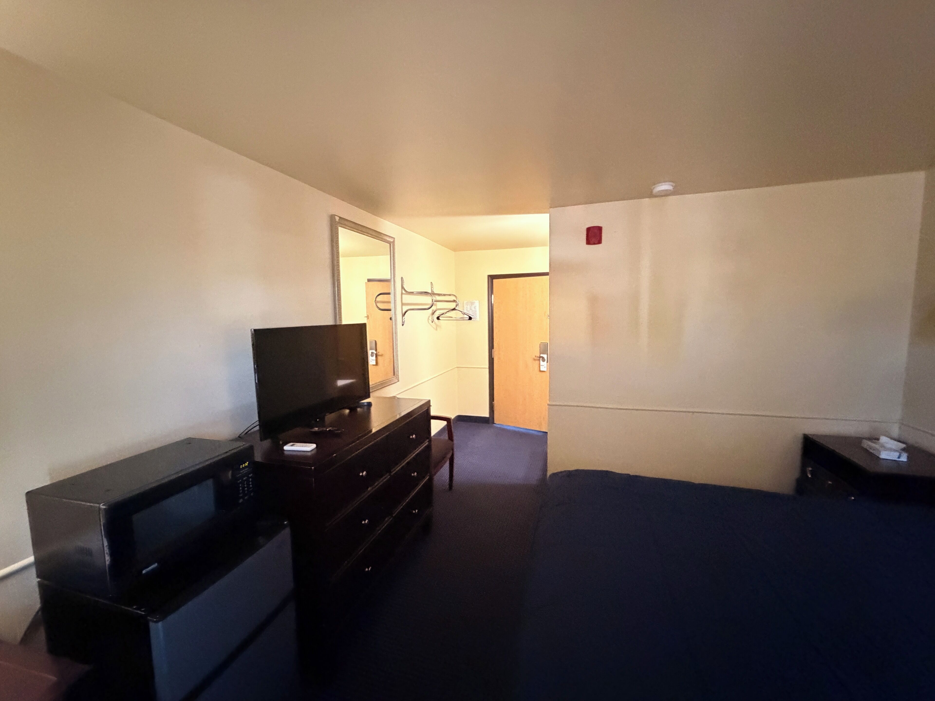 Habitación de hotel con televisión en una cómoda, espejo, puerta y cama.