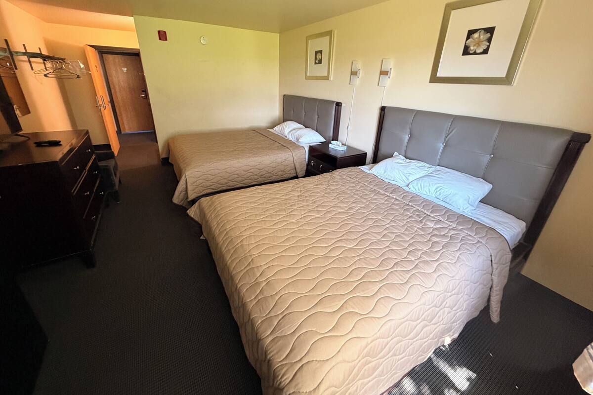 A hotel room with two beds, a dresser, a nightstand, and a door.