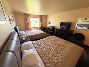 A hotel room with two beds, a desk, a chair, a television, and a window with curtains. - East Grand Inn Grand Forks ND I 29 (East Grand Forks)