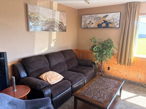 A living room with a dark brown sofa, a coffee table, a potted plant, and two abstract paintings on the wall. - East Grand Inn Grand Forks ND I 29 (East Grand Forks)