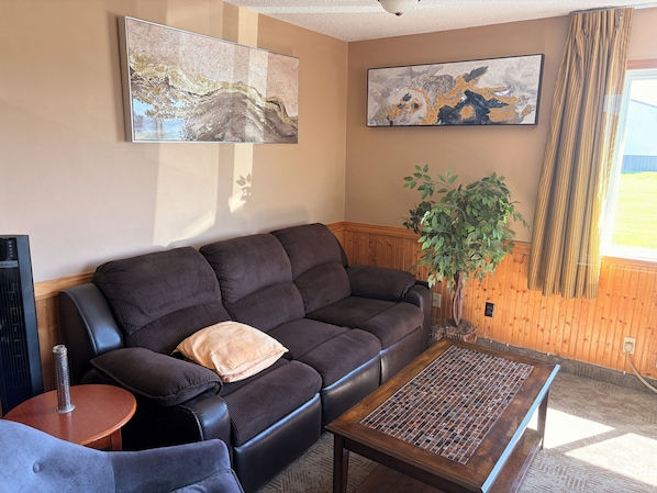 A living room with a dark brown sofa, a coffee table, a potted plant, and two abstract paintings on the wall.