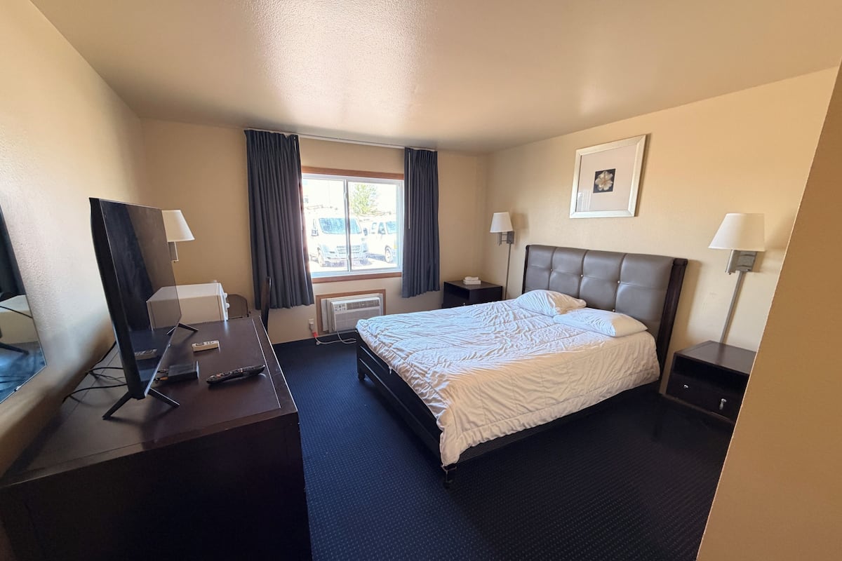 A hotel room with a bed, desk, TV, and window with curtains.