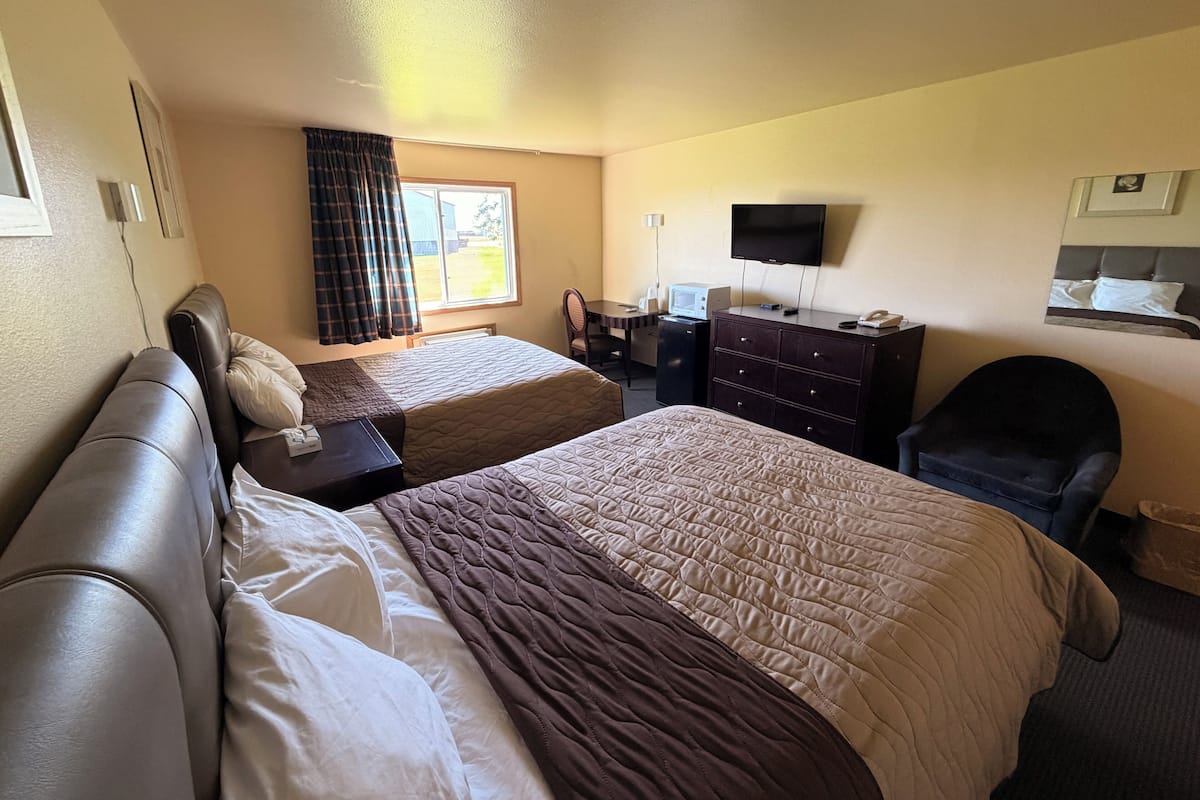 A hotel room with two beds, a desk with a computer, a TV, and a window with curtains.