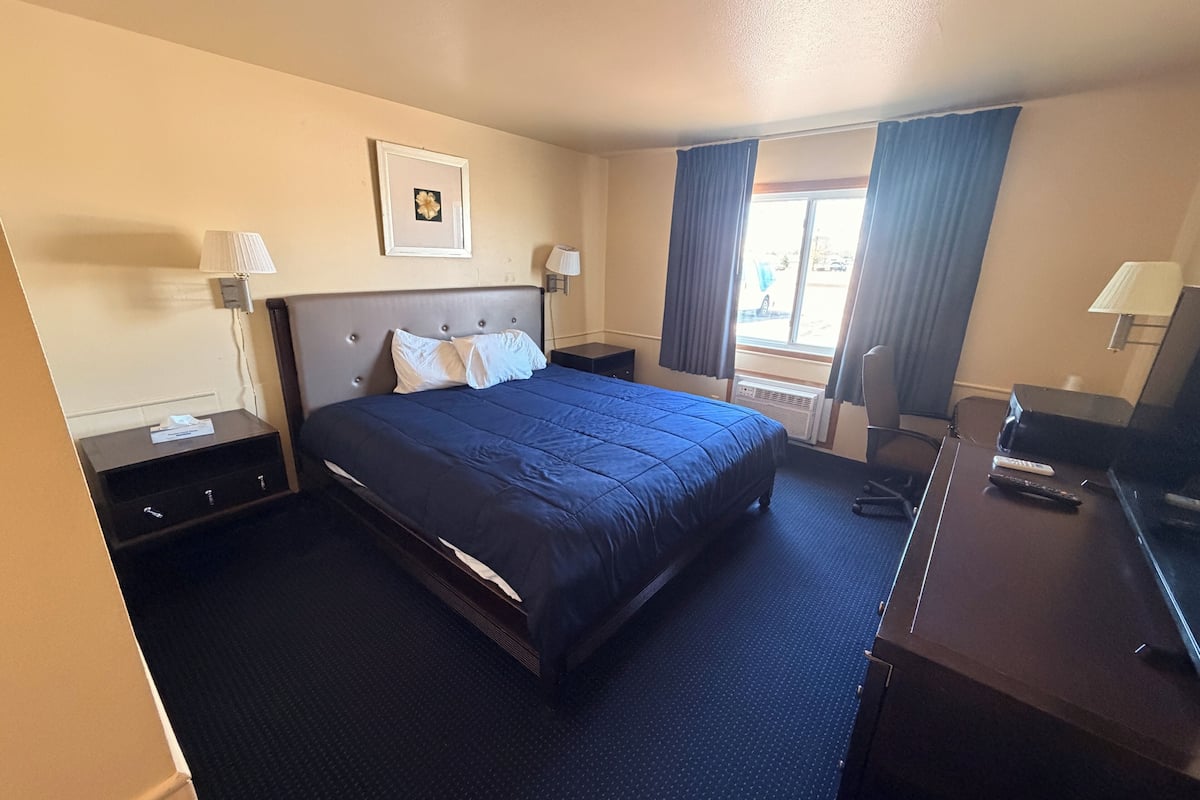 A hotel room with a bed, bedside tables, a desk, a chair, a TV, and a window with curtains.