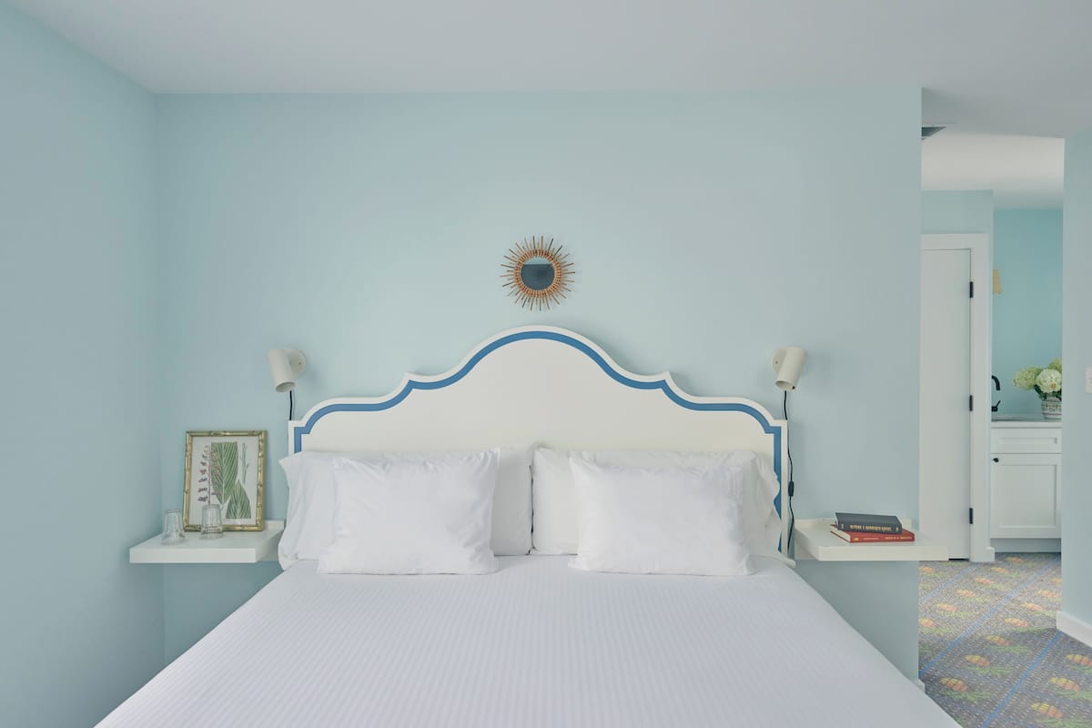 A neatly made bed with white bedding, a blue and white headboard, and a small bedside table with a framed picture and a book.