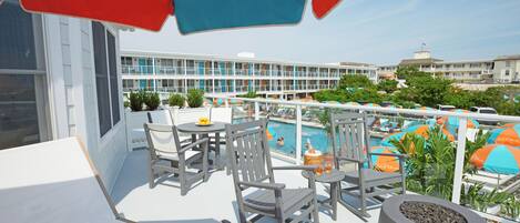 A balcony with outdoor seating, a pool, and a view of a hotel building.