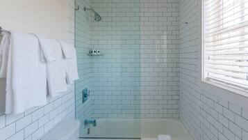 Une salle de bain avec des murs recouverts de carreaux blancs, une douche à parois de verre, une baignoire blanche et des toilettes.