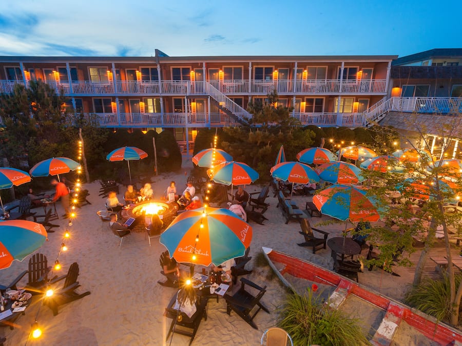 Un hotel frente a la playa con zonas de estar al aire libre, múltiples sombrillas y piscina.
