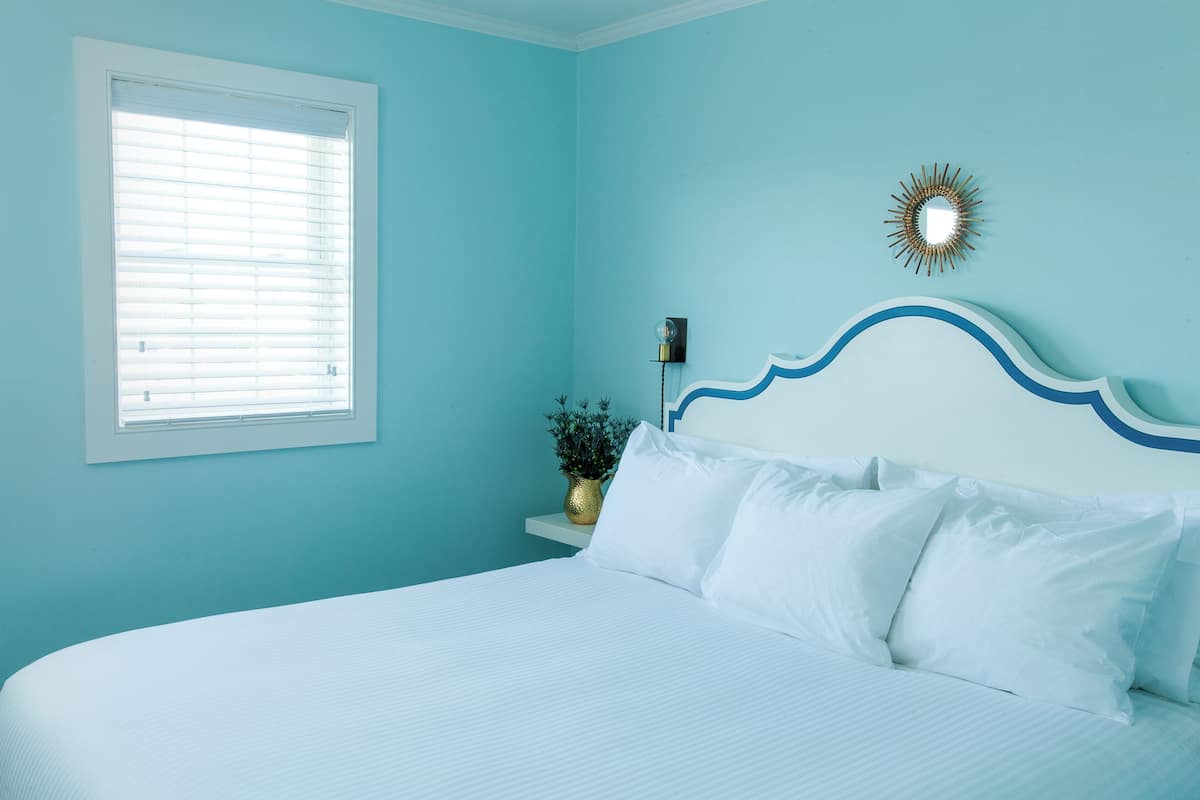 A bedroom with a bed, a window, a wall-mounted lamp, and a decorative mirror.