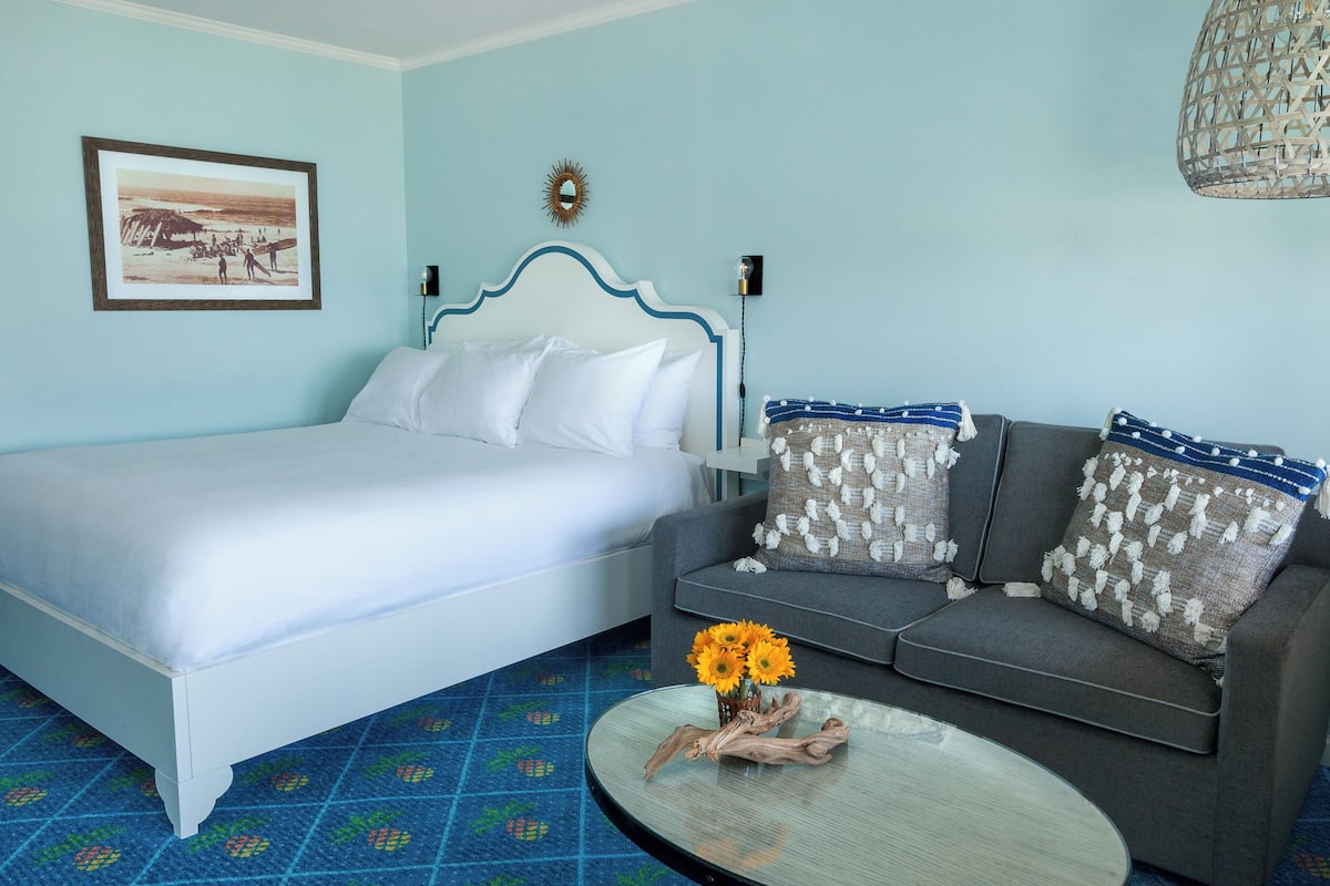 A bedroom with a bed, a sofa, a coffee table, and a wall-mounted lamp.