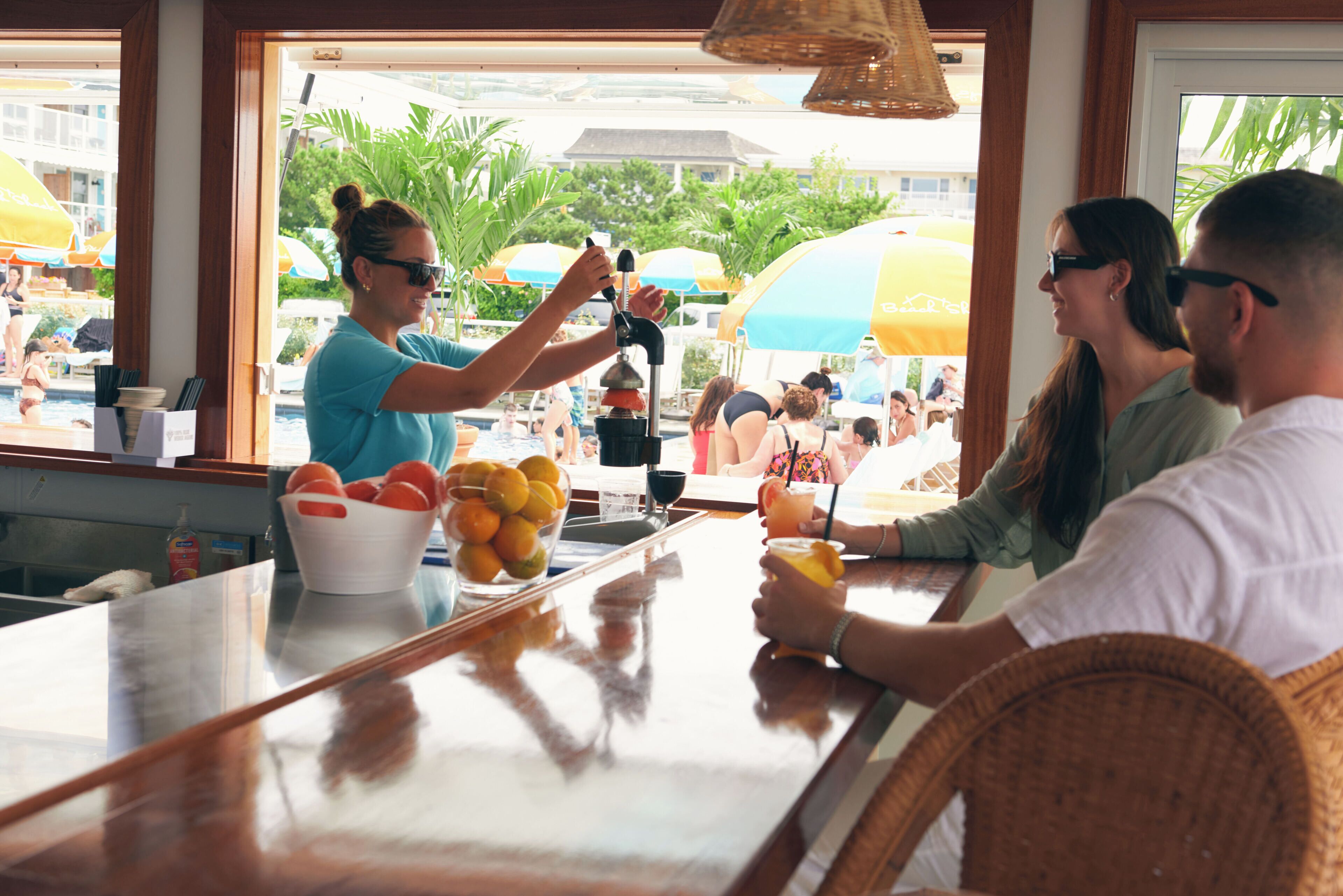 Een bar met een toonbank, een fruitschaal en uitzicht op een zwembadgedeelte met parasols.