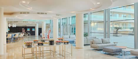 A spacious lobby with a central dining area, seating arrangements, and large windows offering views of the exterior.