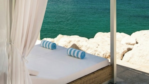Una cama frente al mar con dosel blanco, almohadas blancas y vistas al océano.
