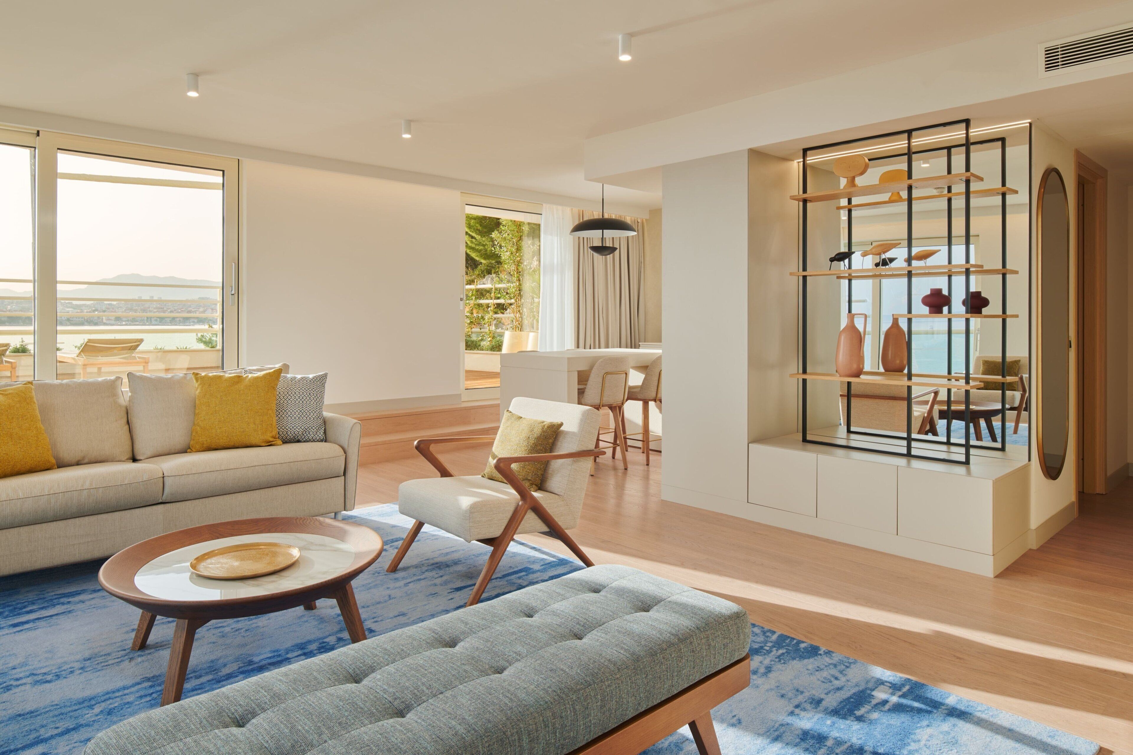 Ein modernes Wohnzimmer mit Sofa, Sessel und Hocker, ein Essbereich mit Tisch und Stühlen sowie eine Vitrine mit Dekorationselementen.