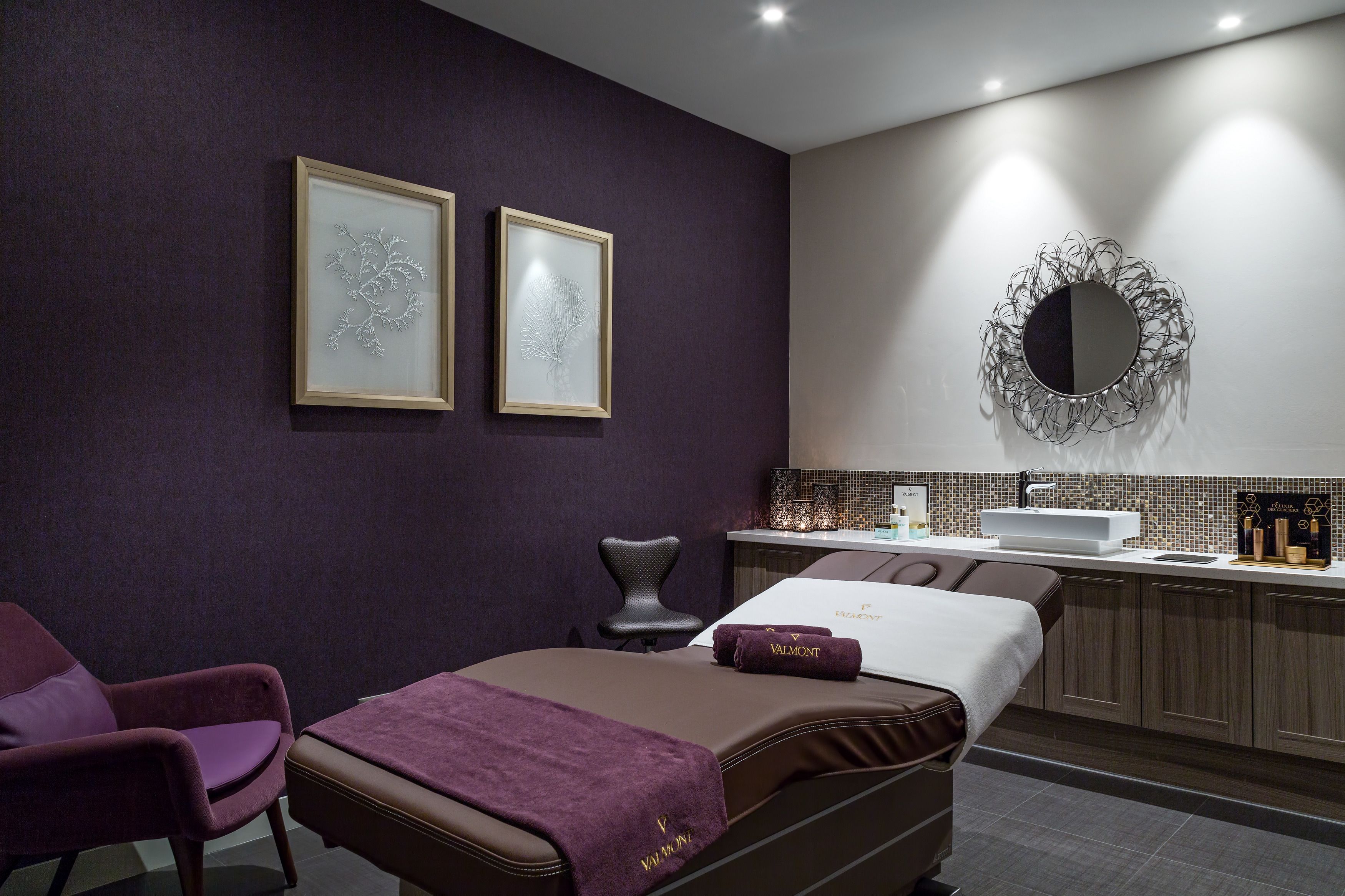 Een moderne spa ruimte met een massagetafel, een stoel, een wastafel en twee ingelijste kunstwerken aan de muur.