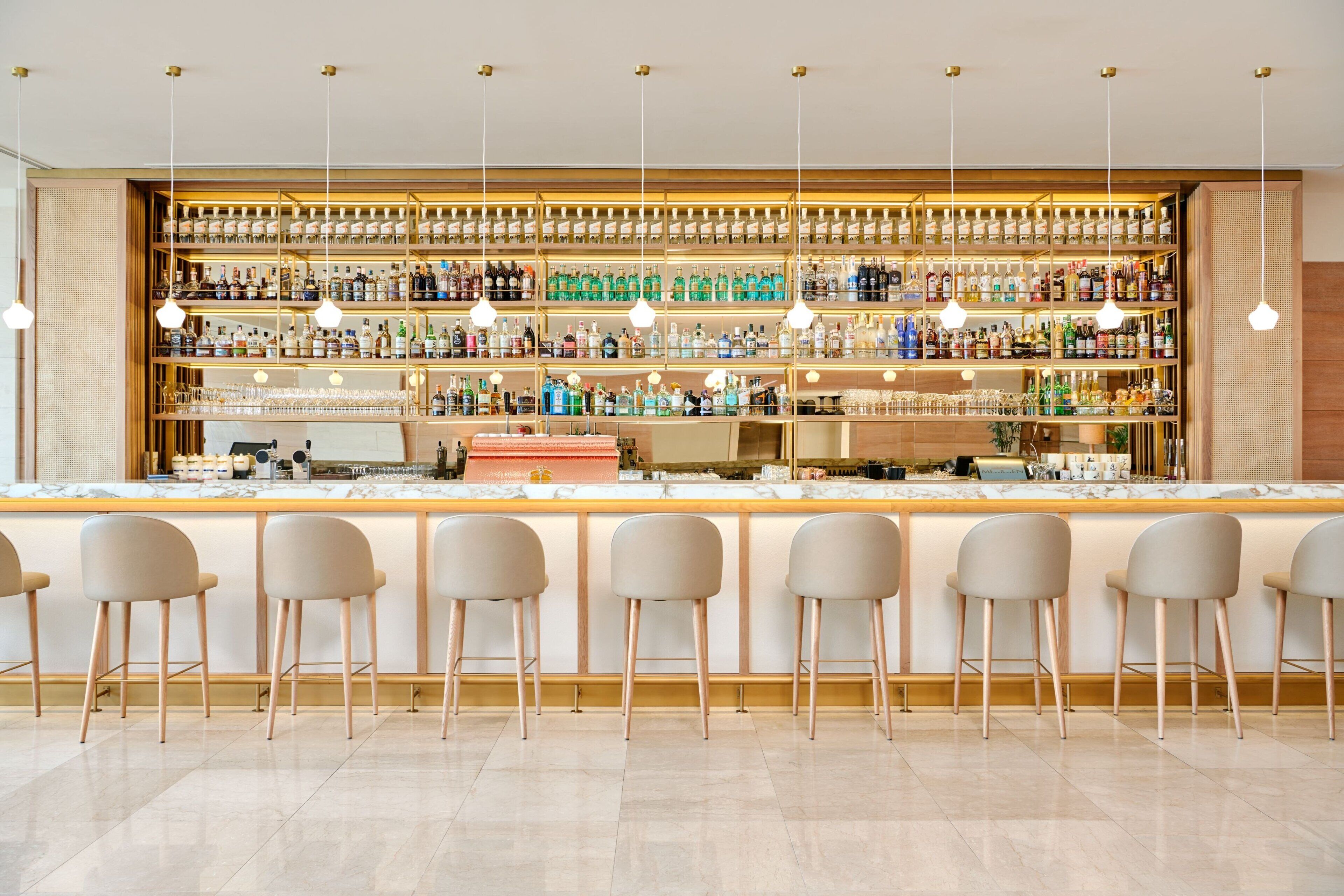 Een bar met meerdere flessenplanken, barstoelen en hangende吊り下げ型ライト.
