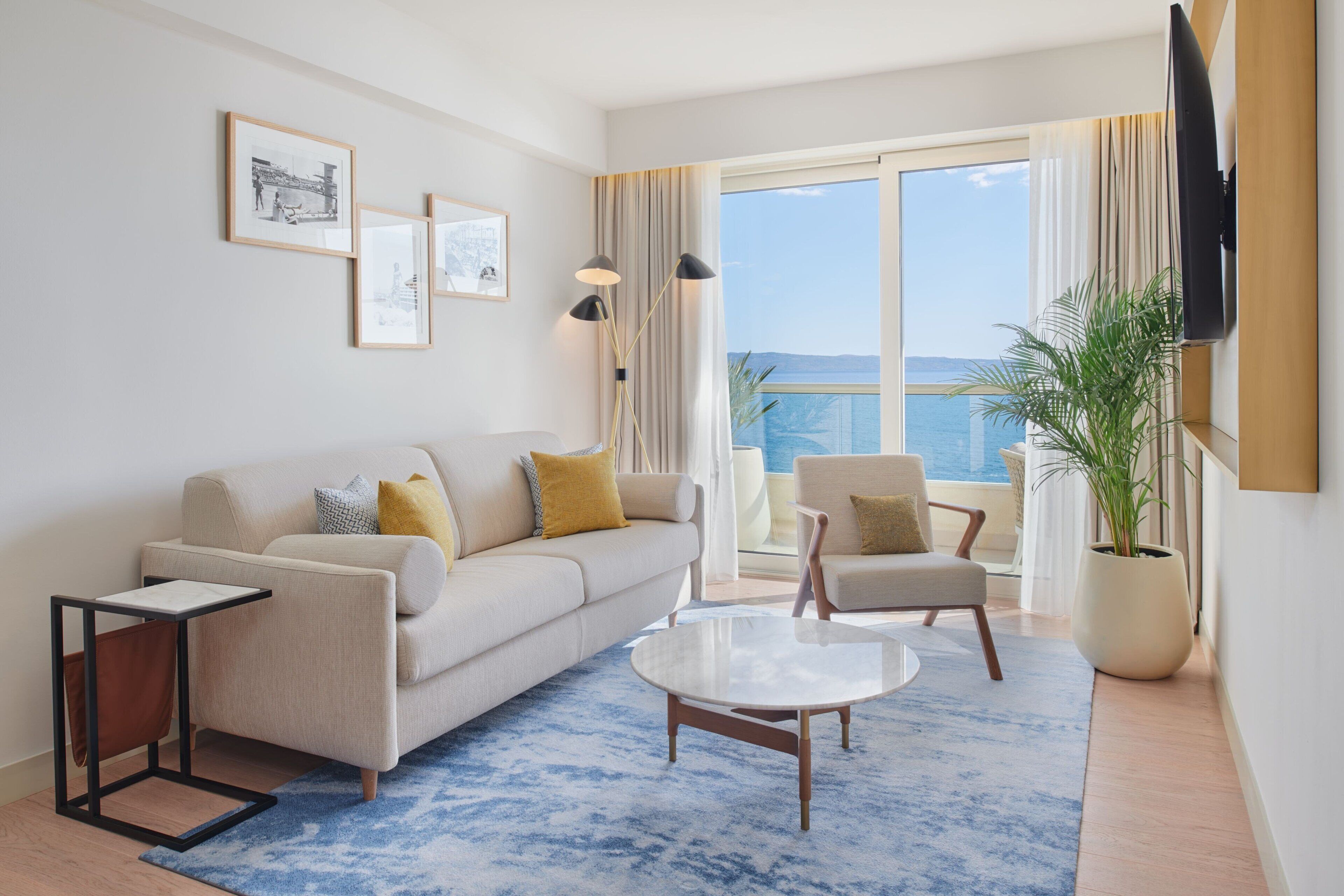 Een moderne woonkamer met een bank, fauteuils, een salontafel en een groot raam met uitzicht op zee.