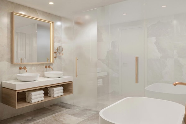 A modern bathroom with two sinks, a large mirror, and a freestanding bathtub.