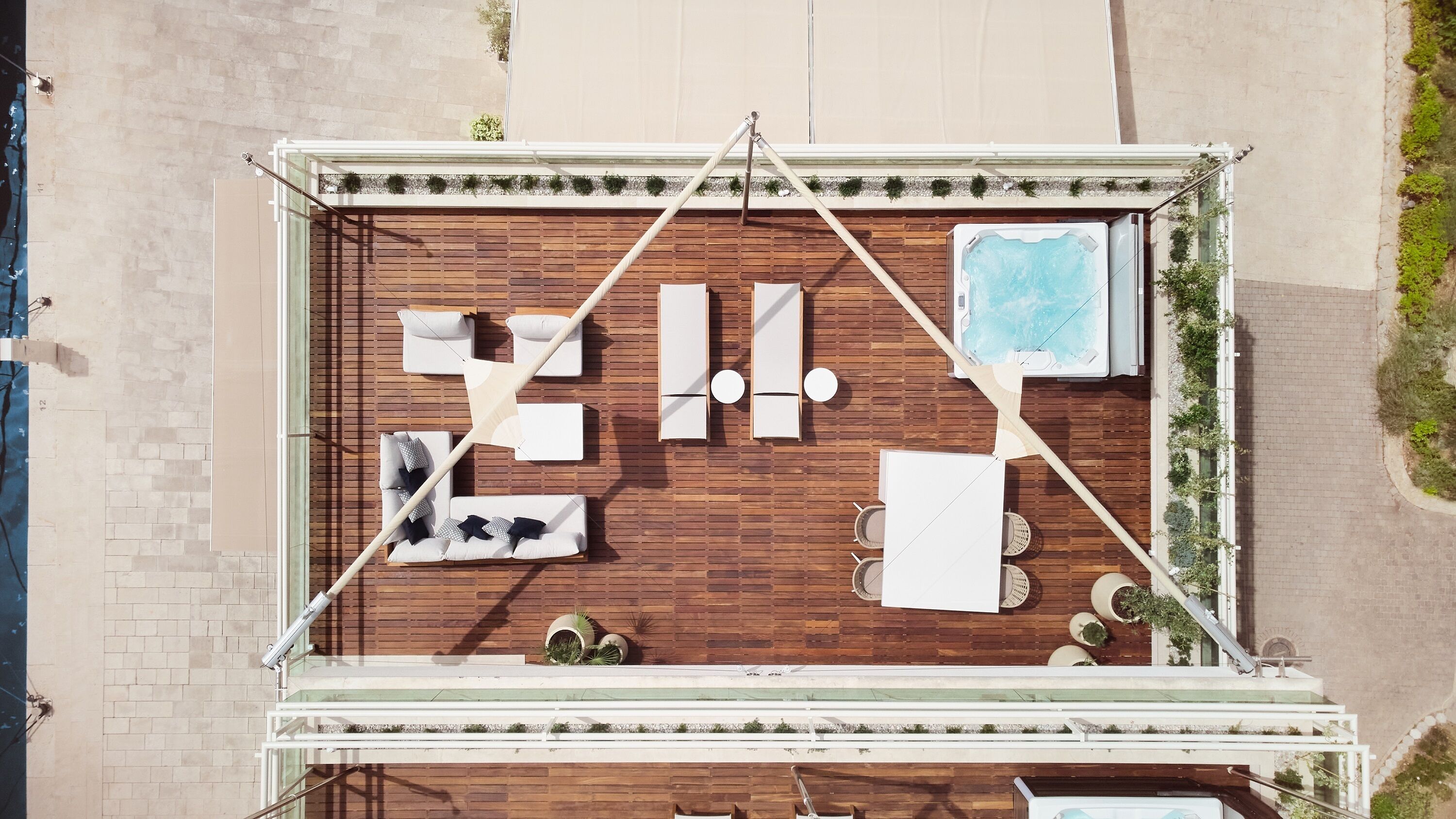 Une terrasse sur le toit avec une plateforme en bois, des chaises longues blanches, un jacuzzi et des plantes en pot.