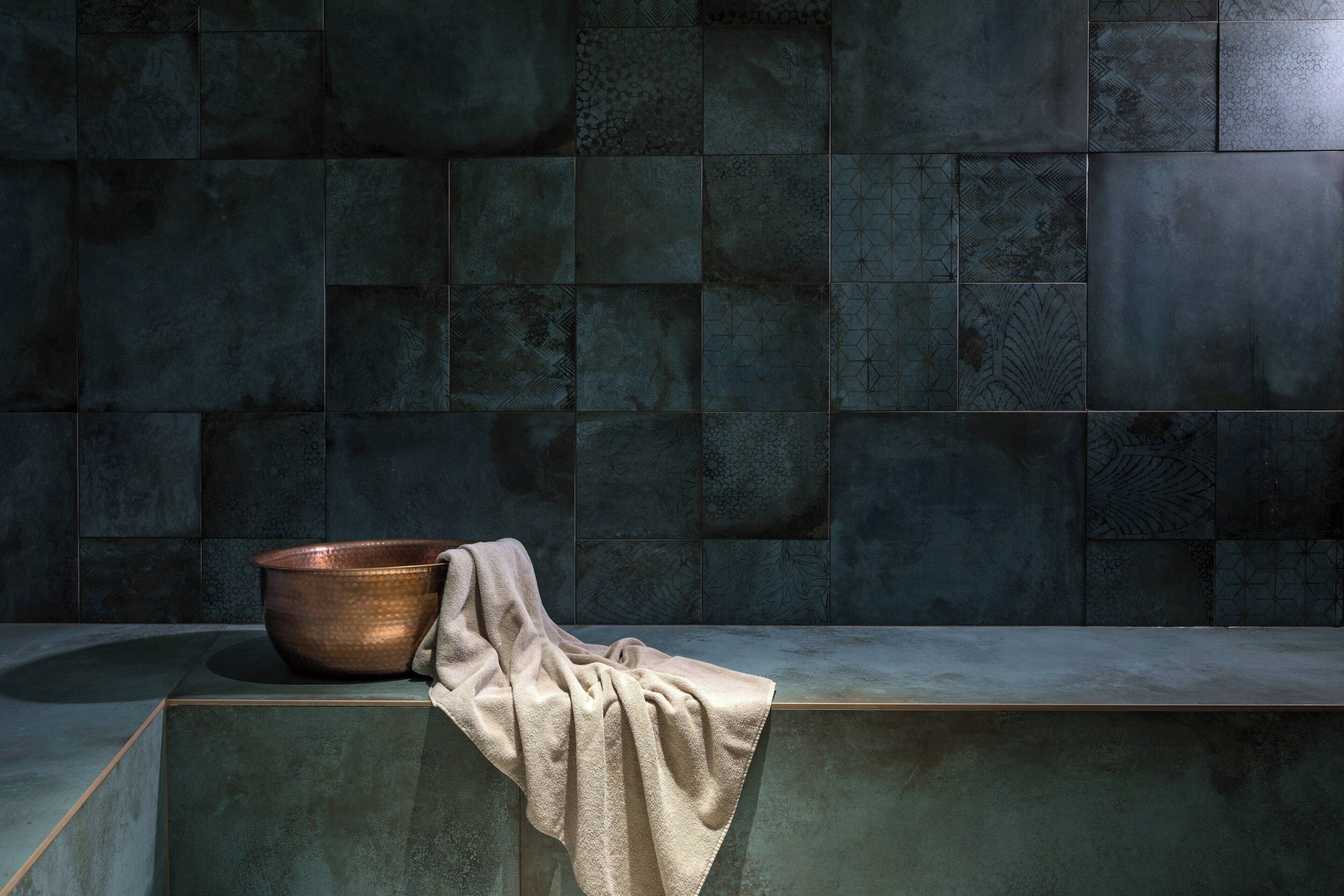A bathroom with a large, dark, textured tile wall and a single copper basin on a beige countertop.