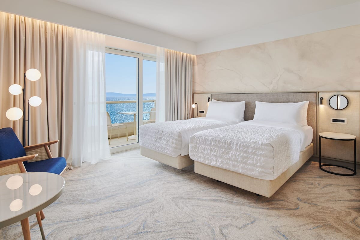 A hotel room with two beds, a balcony with a view, a round table, and a chair.