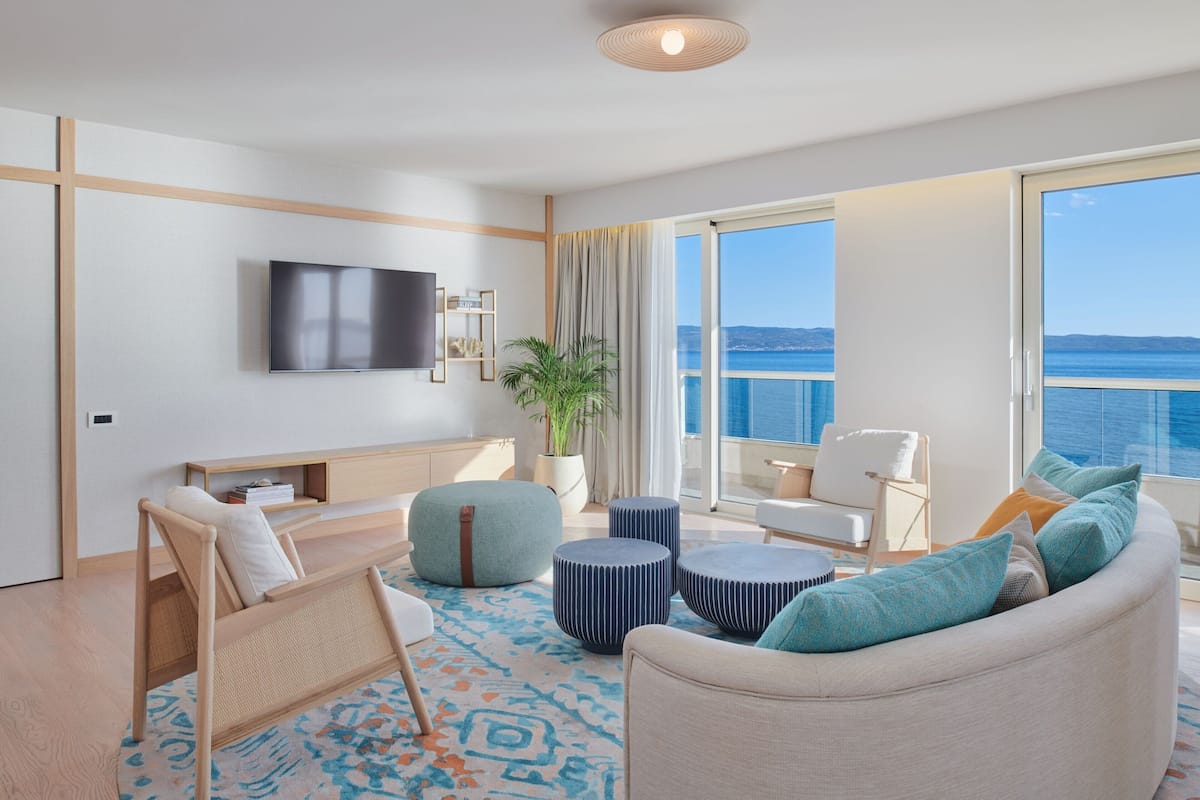 A modern living room with a large TV, comfortable seating, a view of the sea, and a balcony.
