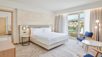 Een hotelkamer met een groot bed, een bureau, een stoel en een balkon met uitzicht op de stad.