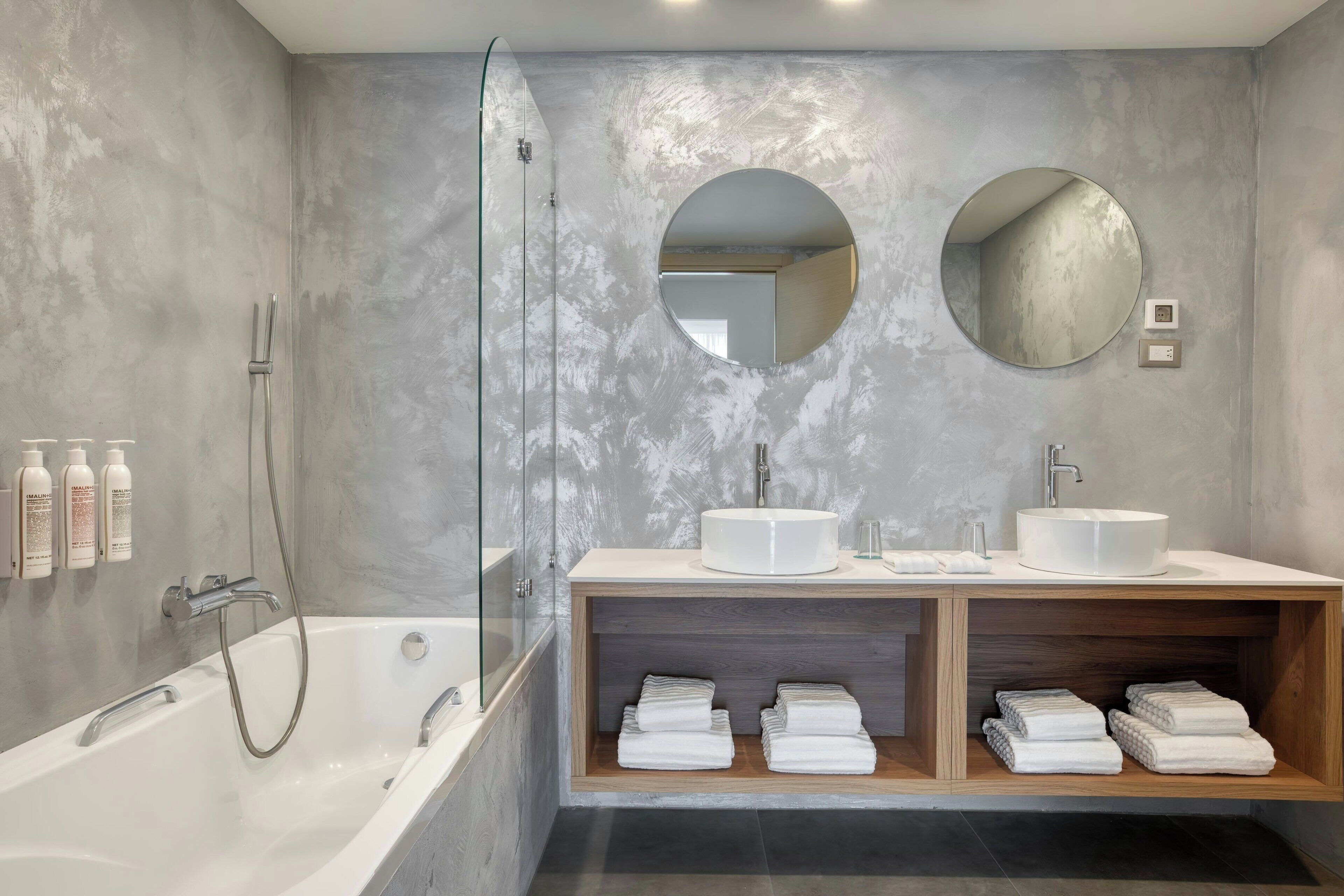 A modern bathroom with a bathtub, two sinks, and a shower. There are towels and toiletries on the vanity.