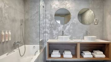 A modern bathroom with a bathtub, two sinks, and a shower. There are towels and toiletries on the vanity.