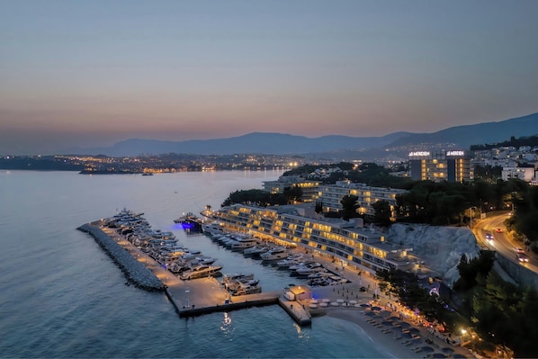 A marina with boats docked, a hotel with multiple floors, and a coastal cityscape in the background.