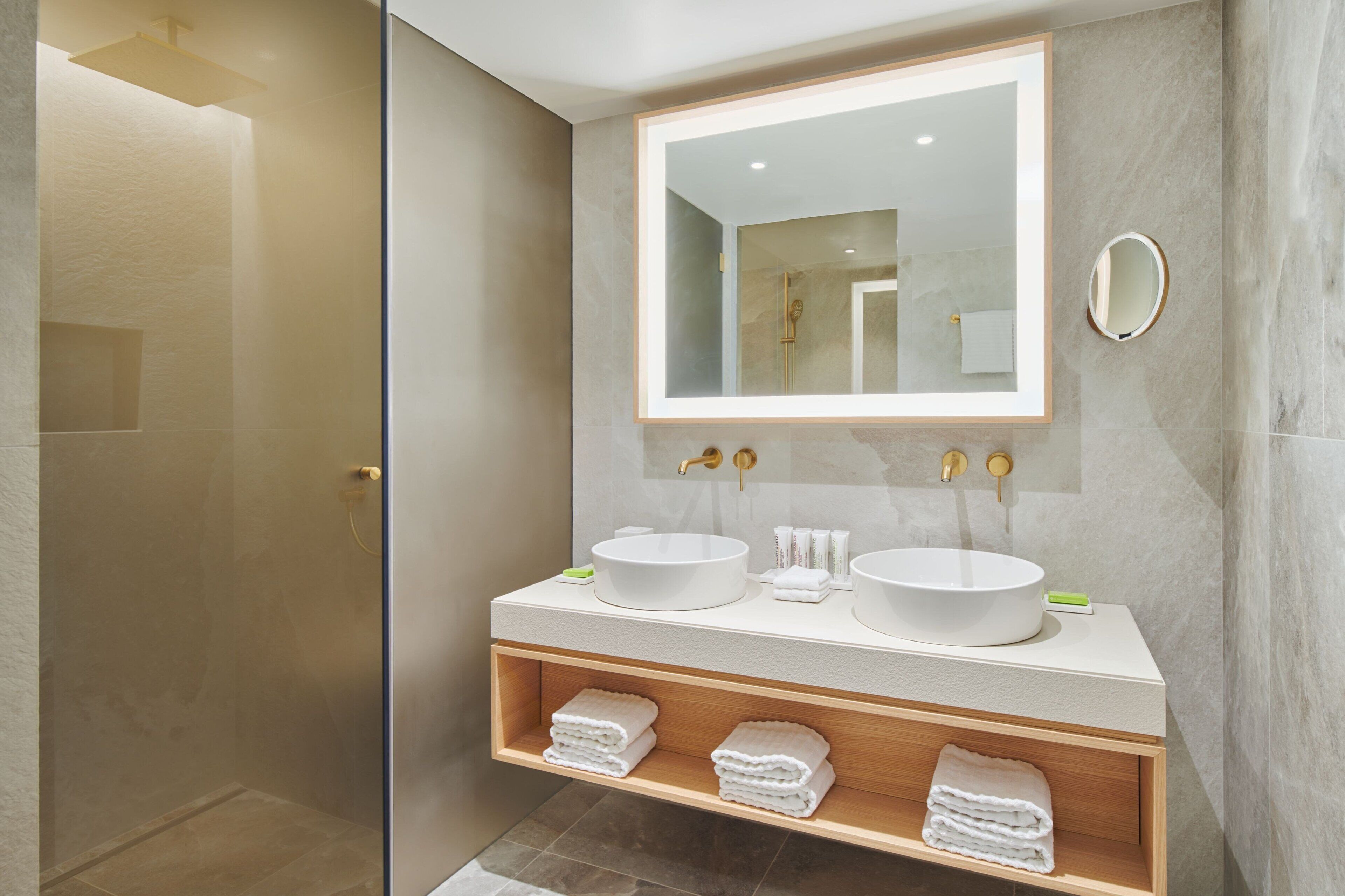 A modern bathroom with two sinks, a large mirror, and a glass shower enclosure.