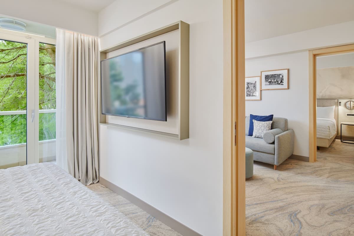 A modern hotel room with a large bed, a flat-screen TV mounted on the wall, a sofa with a cushion, and a desk with a chair.