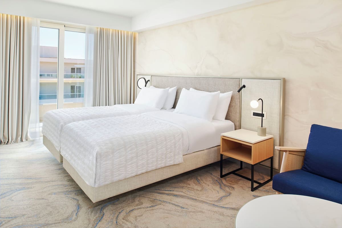 A hotel room with a large bed, a desk, a chair, and a view of a building through the window.