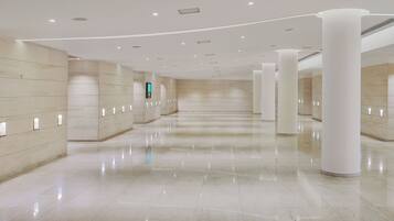 Een ruime, moderne lobby met een gepolijste marmeren vloer, witte zuilen en inbouwverlichting.