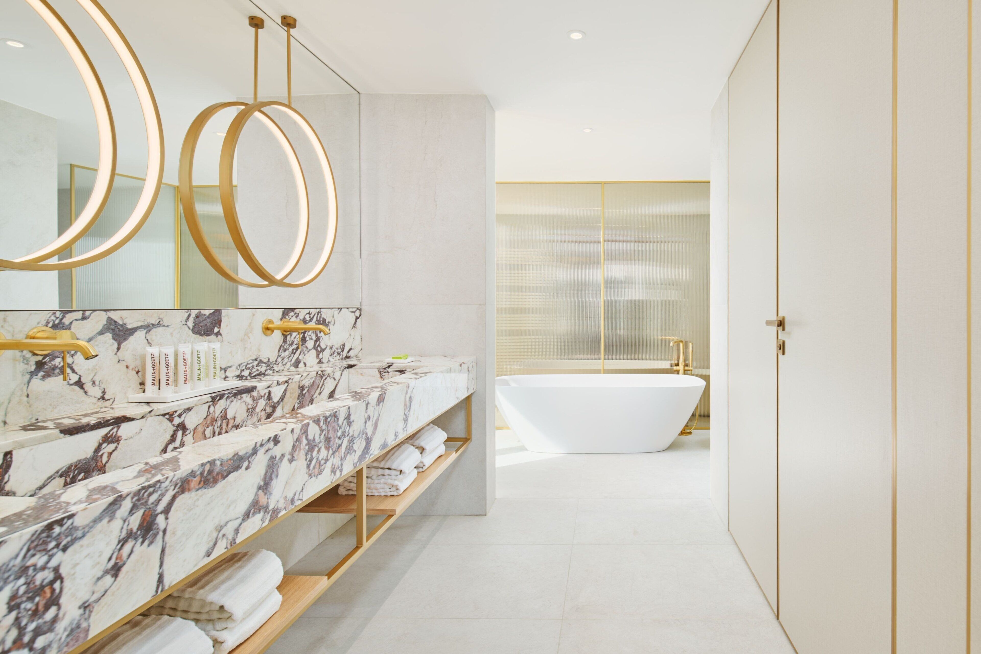 Ein modernes Badezimmer mit Waschtisch aus Marmor, einer freistehenden Badewanne und goldenen Armaturen.