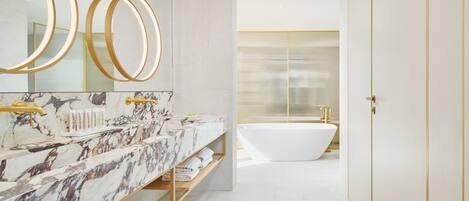 Ein modernes Badezimmer mit Waschtisch aus Marmor, einer freistehenden Badewanne und goldenen Armaturen.