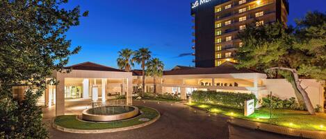 A hotel with a prominent 'MERIDIEN' sign, a landscaped entrance area, and a circular water feature.